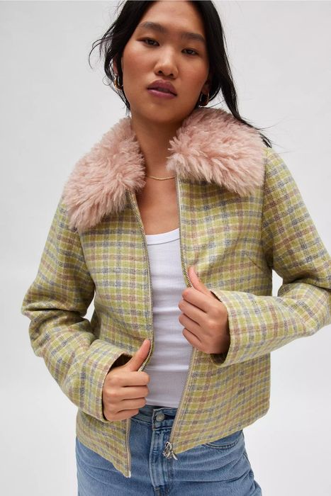 A woman models a plaid jacket with a fluffy collar, paired with a white top and blue jeans, showcasing the outfit for a shopping feature.