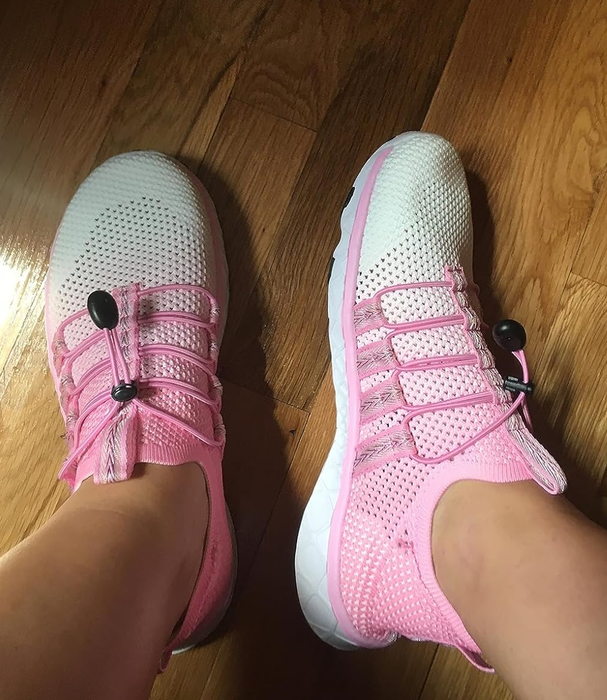 A person wearing white and pink sneakers standing on a wooden floor