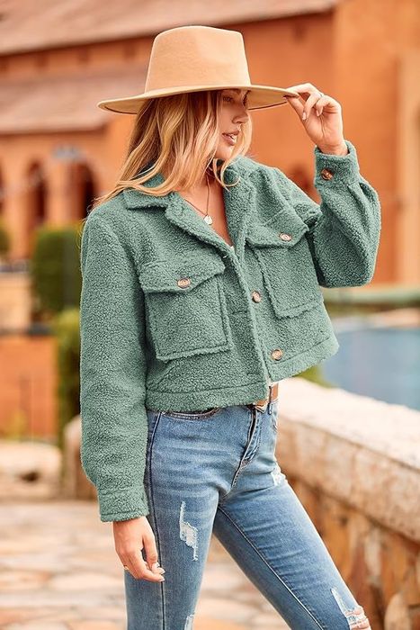 A woman adjusts her tan hat while sporting a textured, button-up jacket and distressed jeans, striking a pose outdoors.