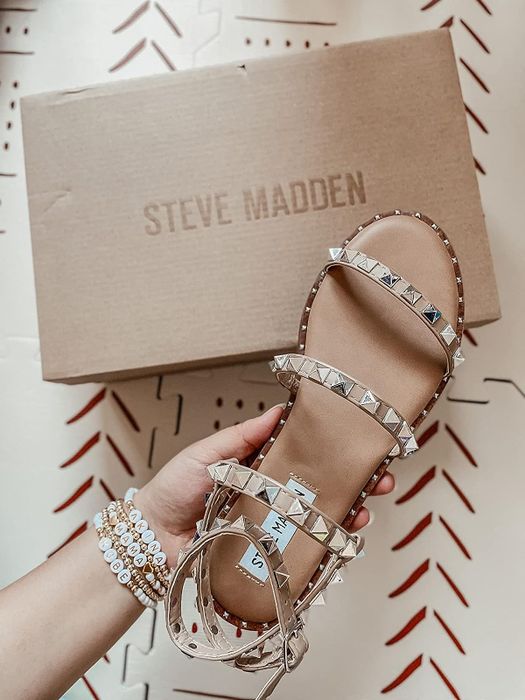 Another reviewer holding sandals with tan straps and studs above the Steve Madden box.