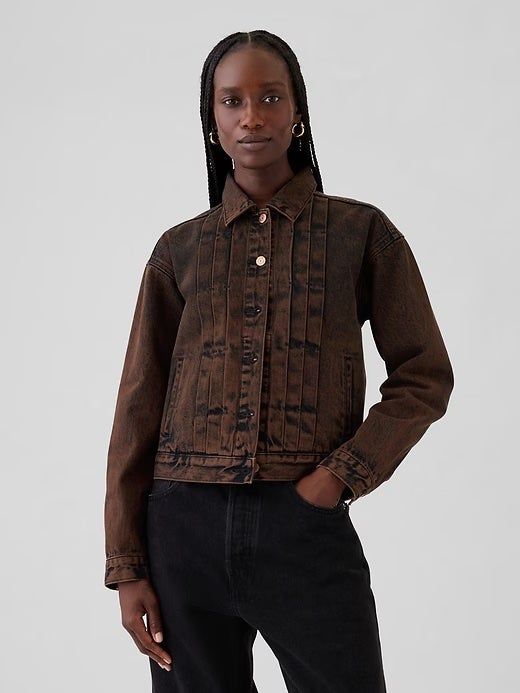 A person models a fashionable denim jacket with vertical seams and dark pants for a shopping-related shot.