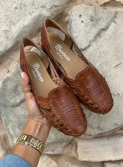 Hand holding a pair of brown woven huaraches