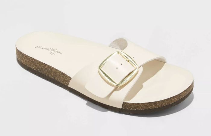 A single cream-colored sandal with a bold buckle detail, displayed on a clean white background.