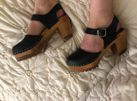 Another reviewer presenting the black clogs, highlighting the stapled leather top, wooden heel, and buckle straps around the ankle