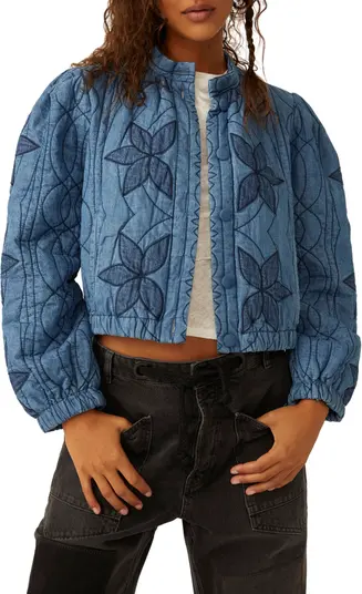 A person showcases a cropped quilted jacket with a floral pattern, paired with sleek black high-waisted pants, combining comfort with style.