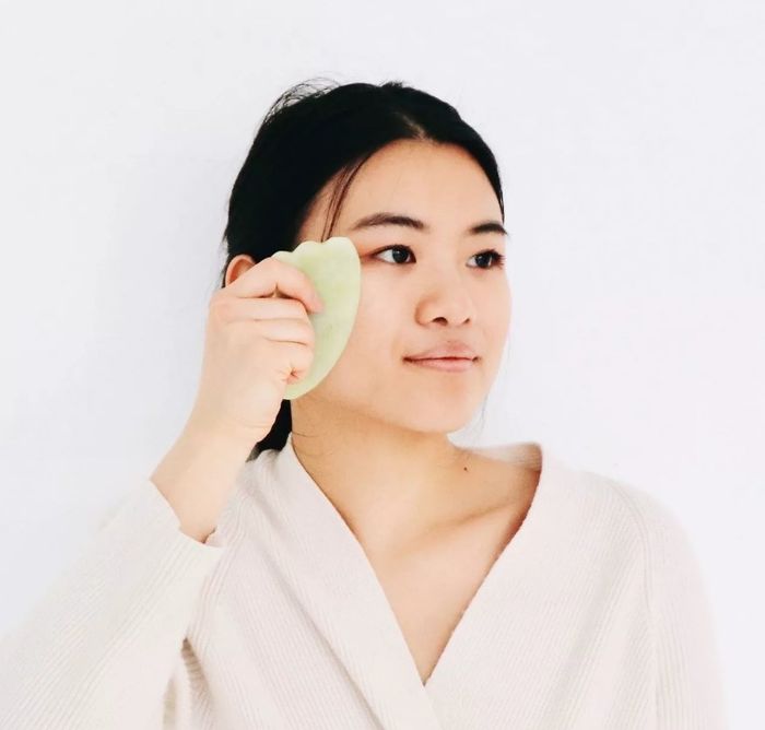 A person using a green Gua Sha facial massaging tool