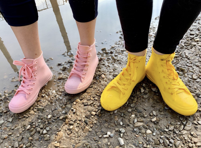 Two reviewers wearing high-top sneaker-style rain shoes in light blue and yellow