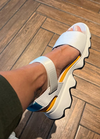 Person trying on chunky white sandals with thick straps and a serrated sole
