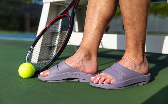 A tennis player wearing lavender-colored Oofos slides.