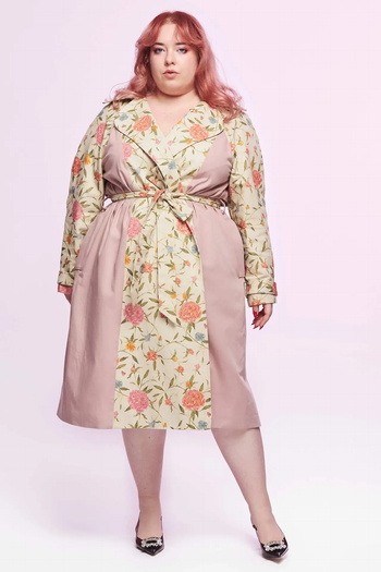 A model wears a floral-patterned trench coat with side panels, striking a pose for a fashion article focused on stylish outerwear.