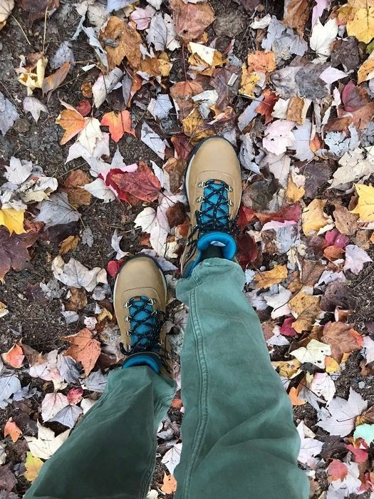 another reviewer wearing beige and dark blue hiking boots while trekking through a leafy autumn landscape