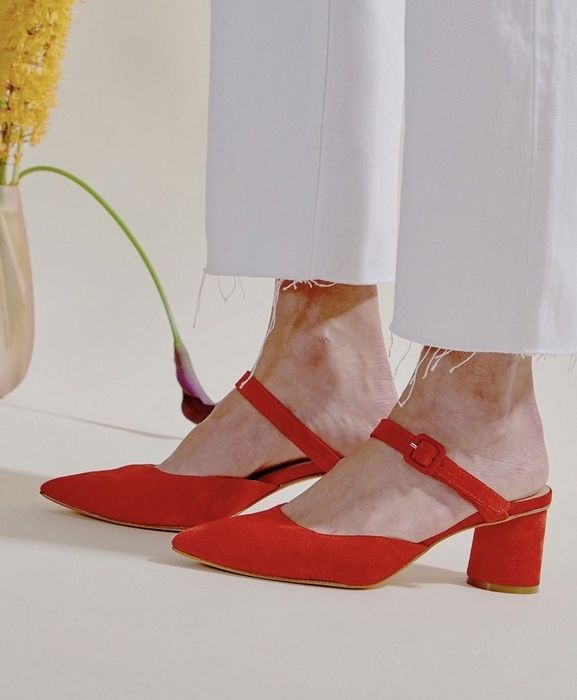 A model in white pants paired with the red suede mules