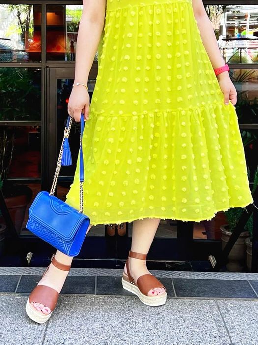 A person wearing a mid-length yellow dress with a blue handbag, paired with brown wedge sandals