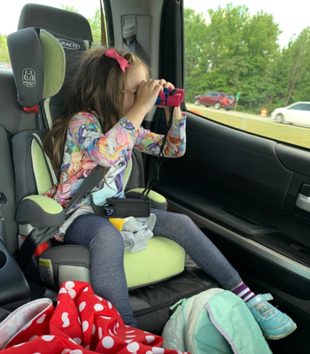 A child in a car seat looking through binoculars, with travel items and clothes scattered around