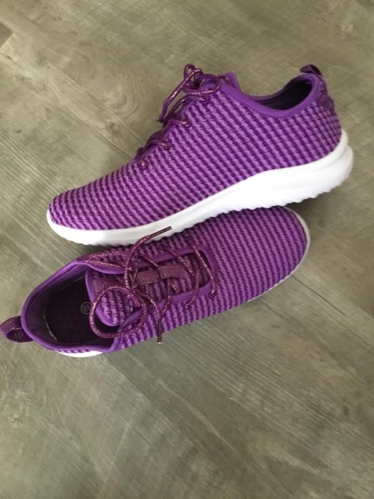 Purple knit sneakers with white soles placed on a grey wooden floor