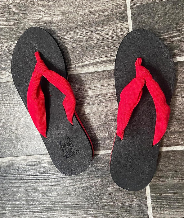 A pair of black flip-flops with red fabric straps, placed on a tiled floor