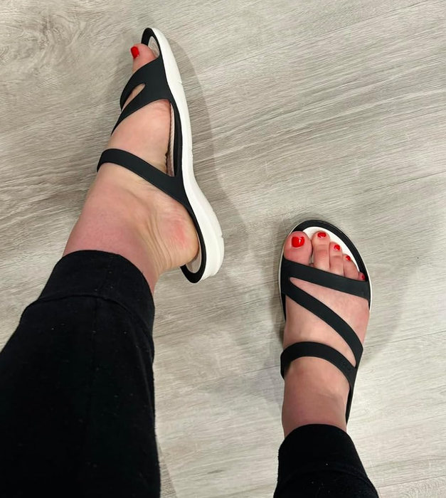 A person wearing black strappy sandals with a white sole