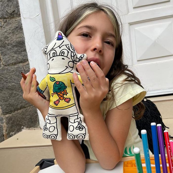 A child holding a hand-drawn, stuffed toy and coloring with markers