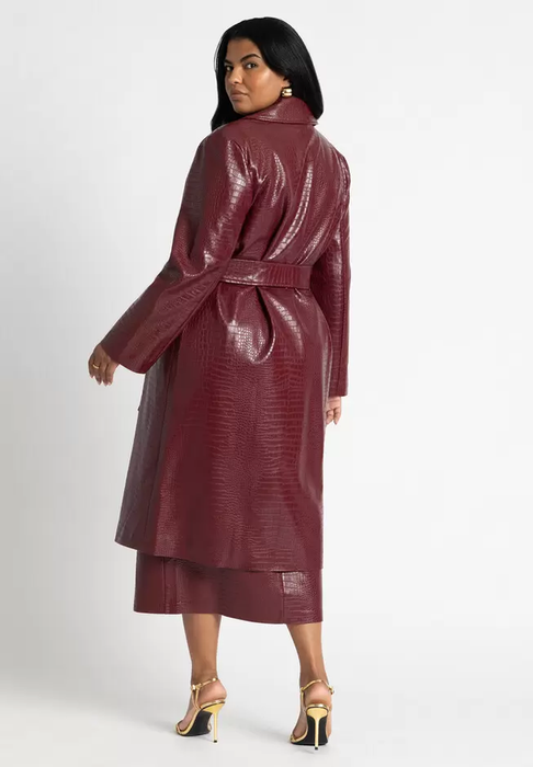 A model strikes a pose in a belted, knee-length textured coat paired with a matching skirt and gold strappy heels.