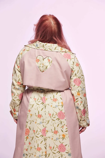 A person wearing a floral trench coat with a heart-shaped cutout on the back, viewed from behind.