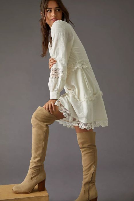 A model rocking sand-colored over-the-knee boots paired with a lace-trimmed dress.