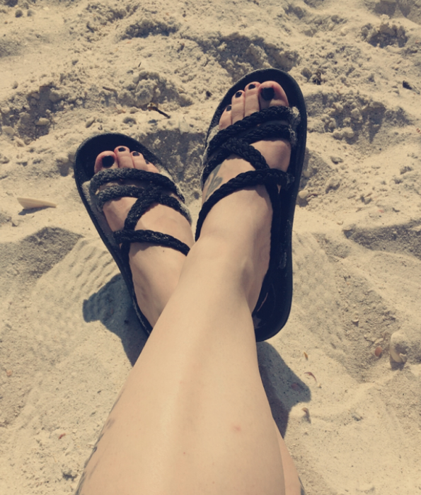 A reviewer wearing black sandals while at the beach.