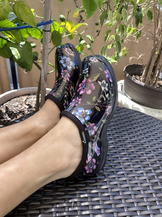 Model wearing black garden shoes with a vibrant blue and pink floral pattern.