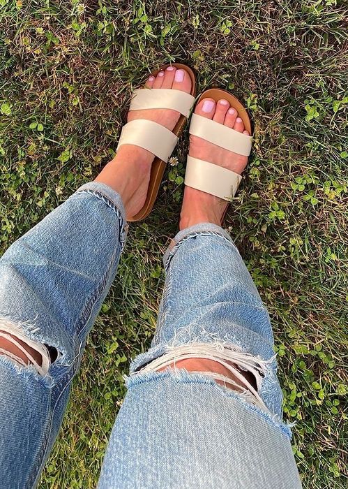 A photo of a person wearing ripped jeans and tan sandals, standing on grass