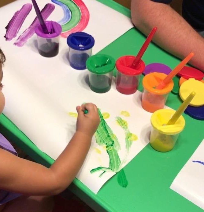 A reviewer’s child painting with the colorful paint cups neatly arranged on the table