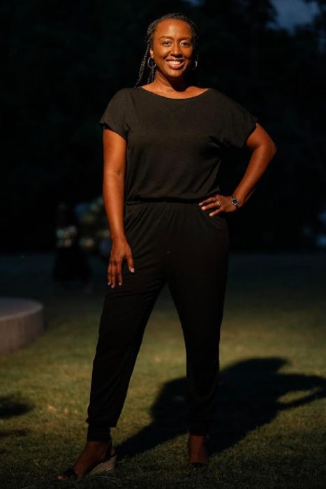 A reviewer posing outdoors at night in a fashionable black jumpsuit.