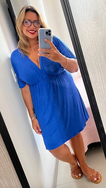 A reviewer wearing a blue knee-length V-neck dress.