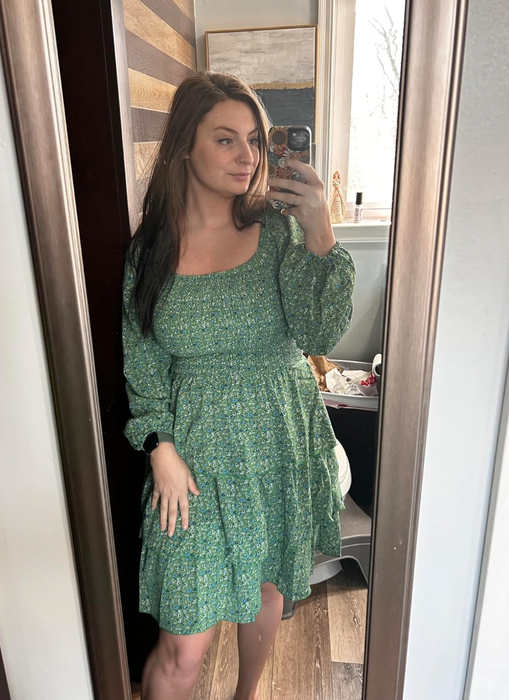 A reviewer in a green patterned dress snaps a selfie in front of a mirror.