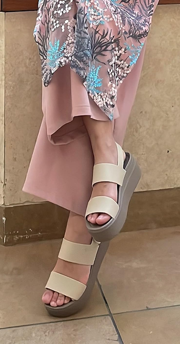 A person in pale pink trousers and a floral-patterned dress, paired with nude platform sandals