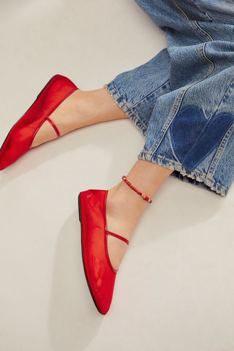 A person wearing jeans and red flat shoes with ankle straps