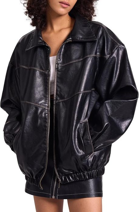 A person dons a black oversized leather jacket, complemented by a matching black leather skirt.