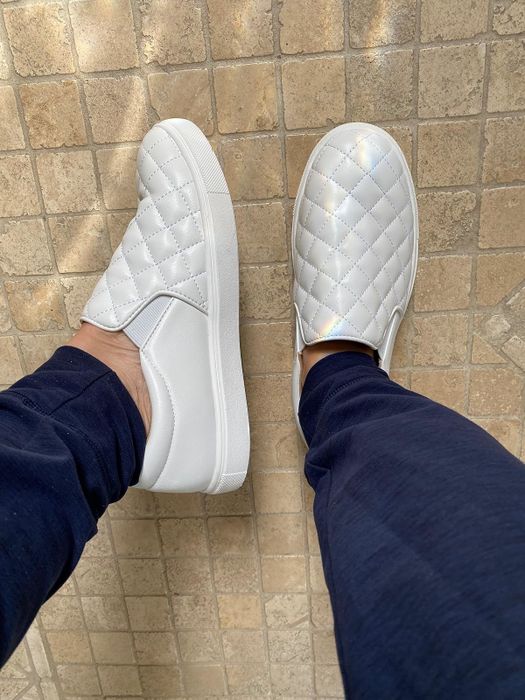 A reviewer wearing white quilted slip-on sneakers.