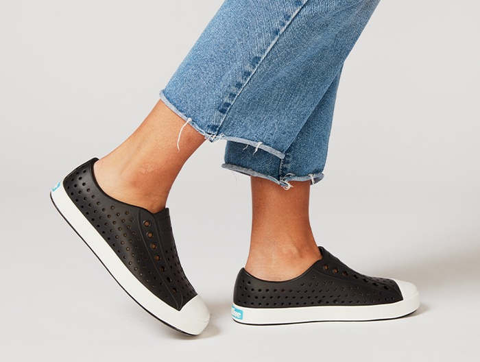 A model wearing black perforated slip-on sneakers with a white toe cap and soles