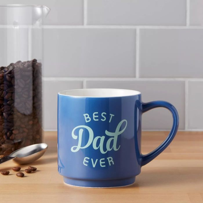 A dark blue mug with 'Best Dad Ever' printed in light blue on the front, resting on a kitchen counter