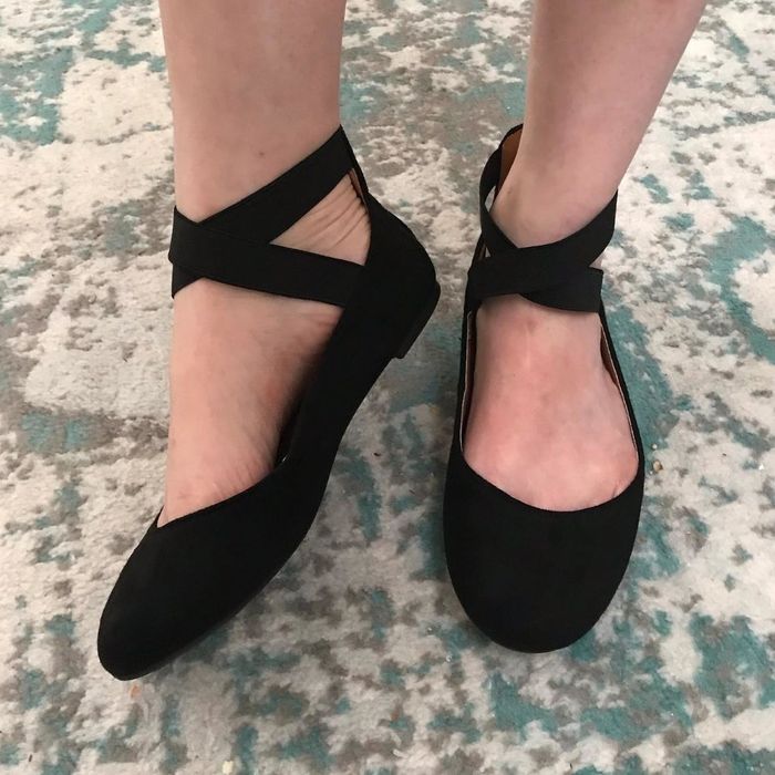 A reviewer photo showcasing a pair of black cross-strap ballerina flats.