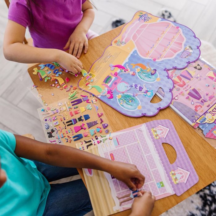 Two children playing with a sticker set that lets them dress up a doll