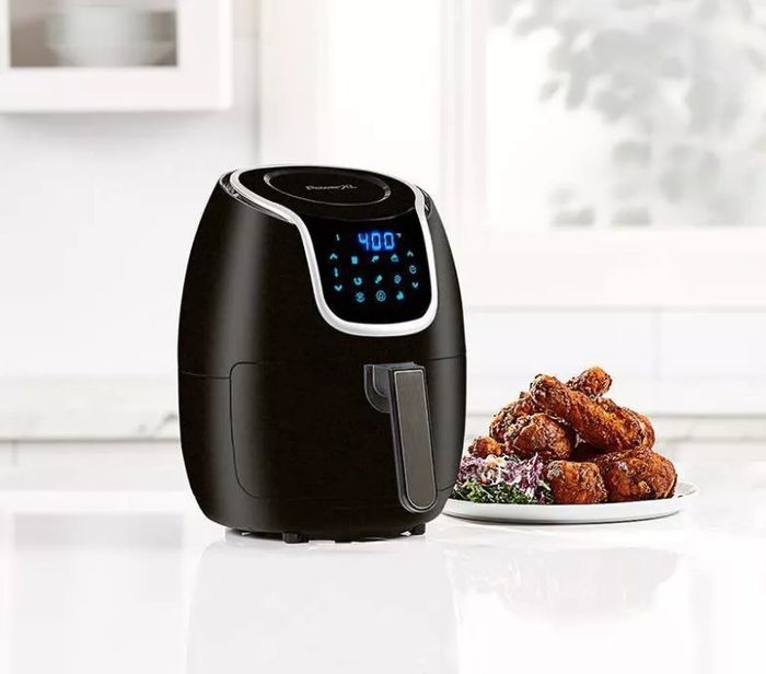 A sleek black air fryer next to a plate of crispy wings on the kitchen counter