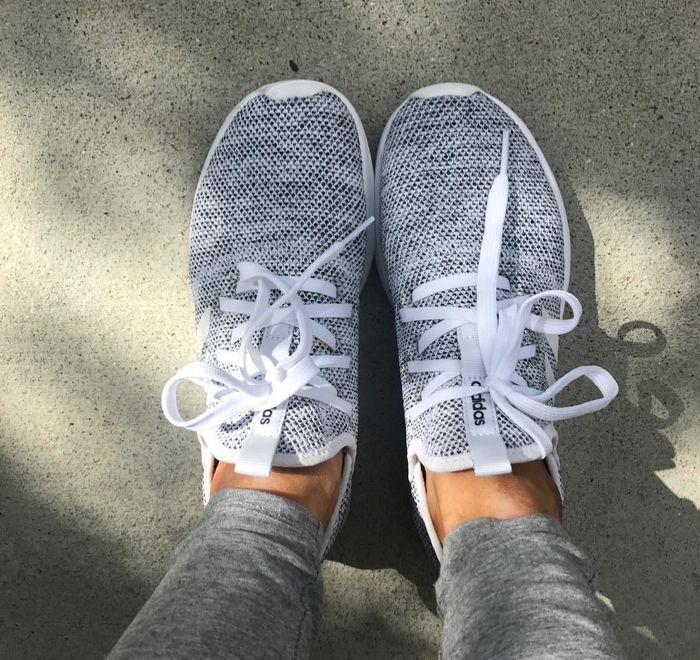 A reviewer showcasing grey Adidas sneakers with white laces, worn outdoors.