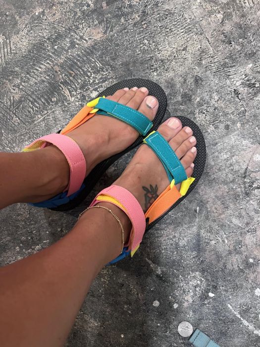 A reviewer wearing vibrant sandals with colorful straps in shades of pink, orange, yellow, and teal.