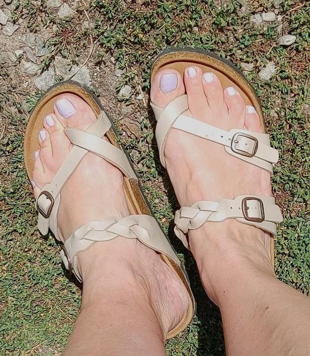 Feet adorned with strap sandals featuring buckles, set against a grassy backdrop, highlighting the style of the footwear
