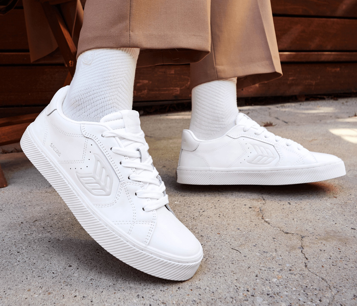 A person wearing white sneakers paired with ribbed socks and tan trousers, walking on pavement