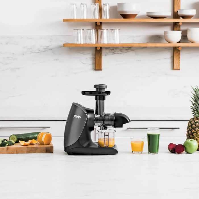 The sleek black juicer sitting on a kitchen countertop, freshly squeezing juice.