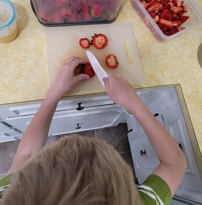 A child safely slices strawberries on a kitchen cutting board, practicing knife skills