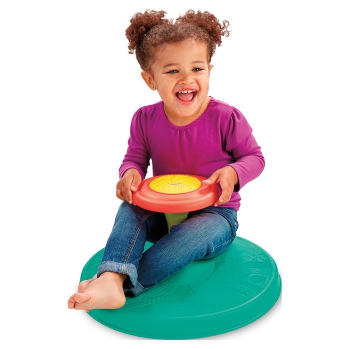 A toddler sitting and spinning on a circular spinning disc.