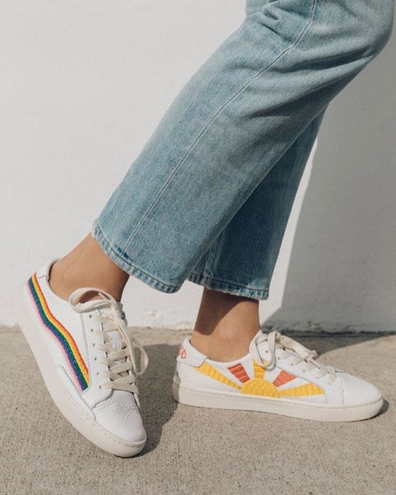 White sneakers adorned with an embroidered rainbow on the sides and a sun design in yellow and orange along the insides.