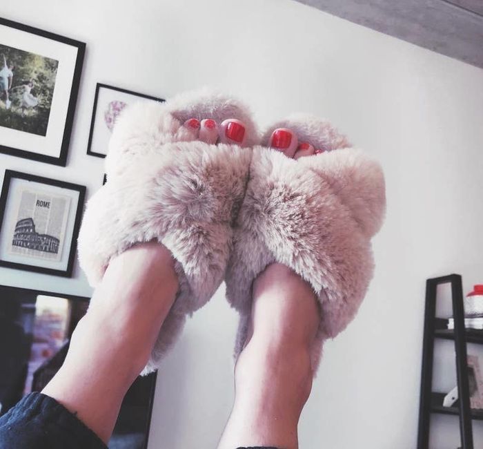 A reviewer showing off the light pink criss-cross fuzzy open-toe slippers.